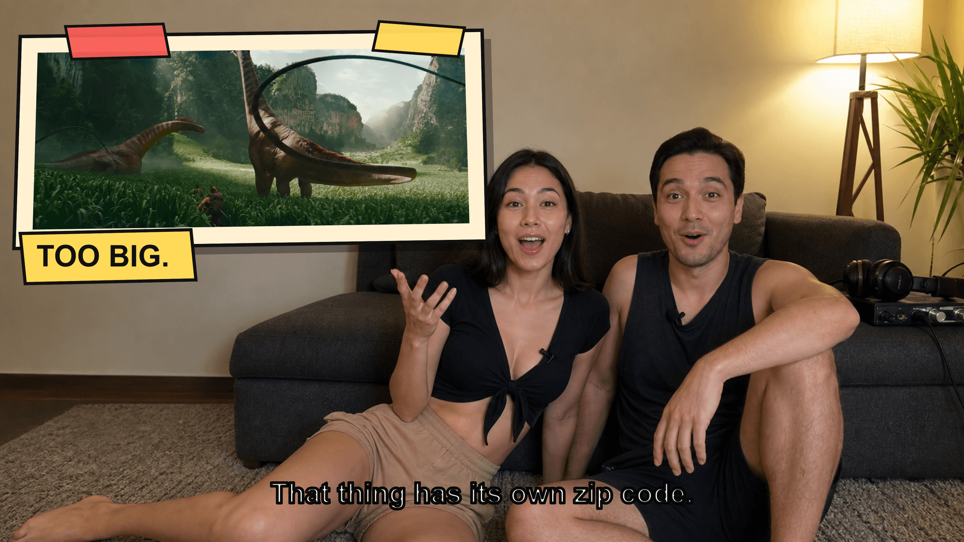 Couple on a couch reacting in shock to a film on a large screen while a camera on a tripod records them